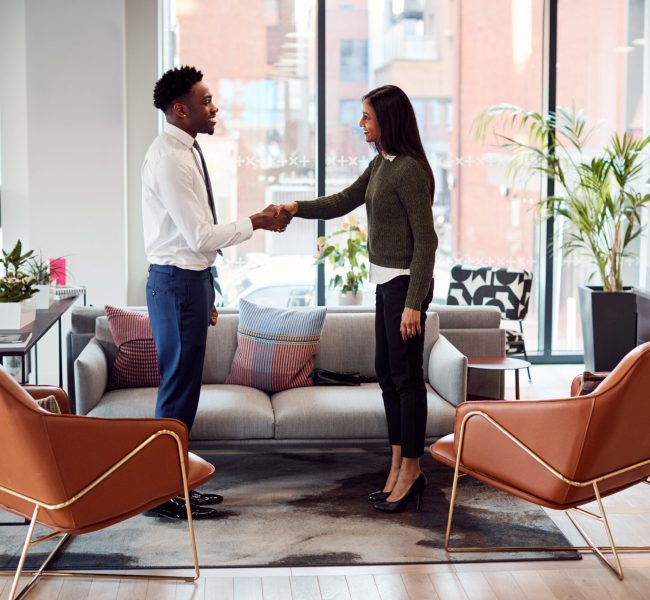 Businesswoman Shaking Hands With Male Interview Candidate In Seating Area Of Modern Office